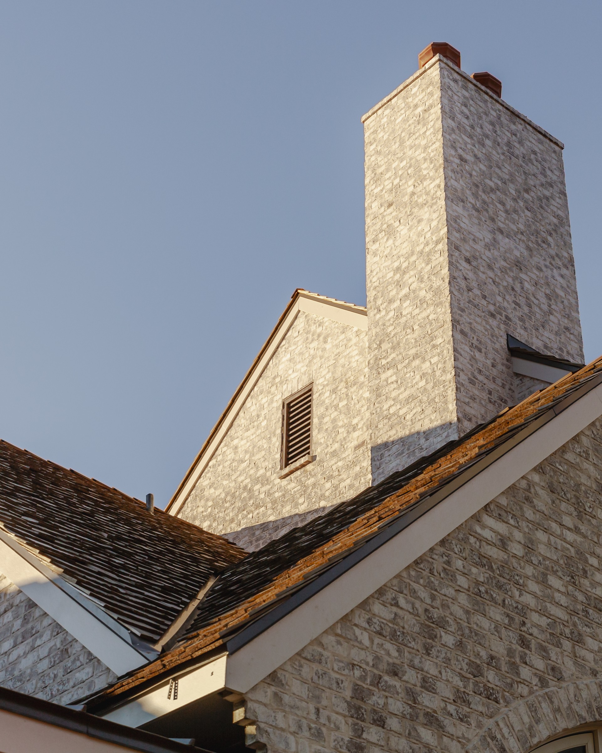 Looking up at the stone gable, chimney and rooflines of a custom home