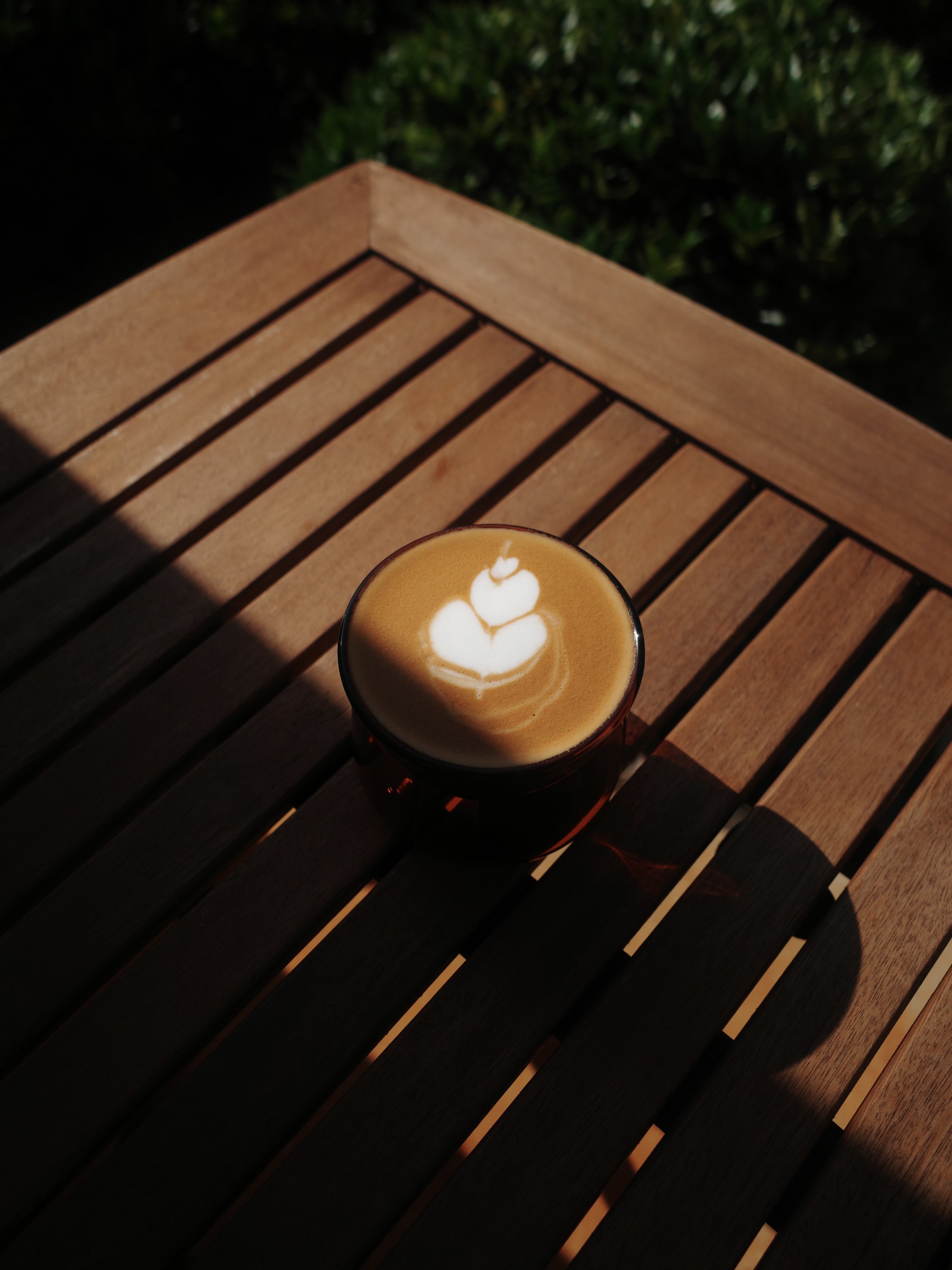 Latte art on a coffee sitting on a sunlit wooden table
