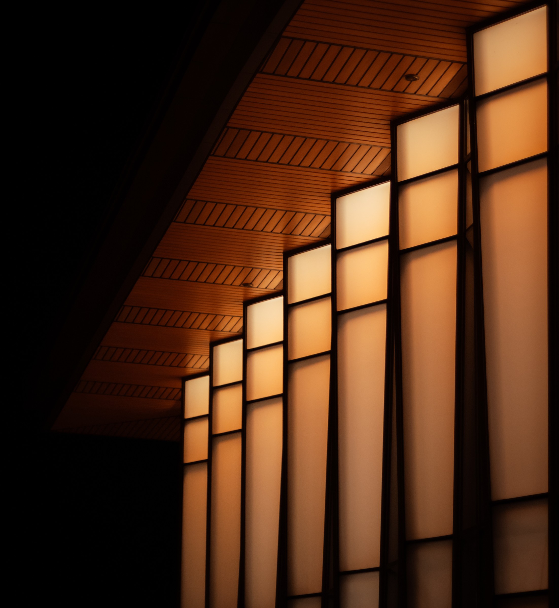 Warm lantern panels glowing along an architectural hallway ceiling and wall