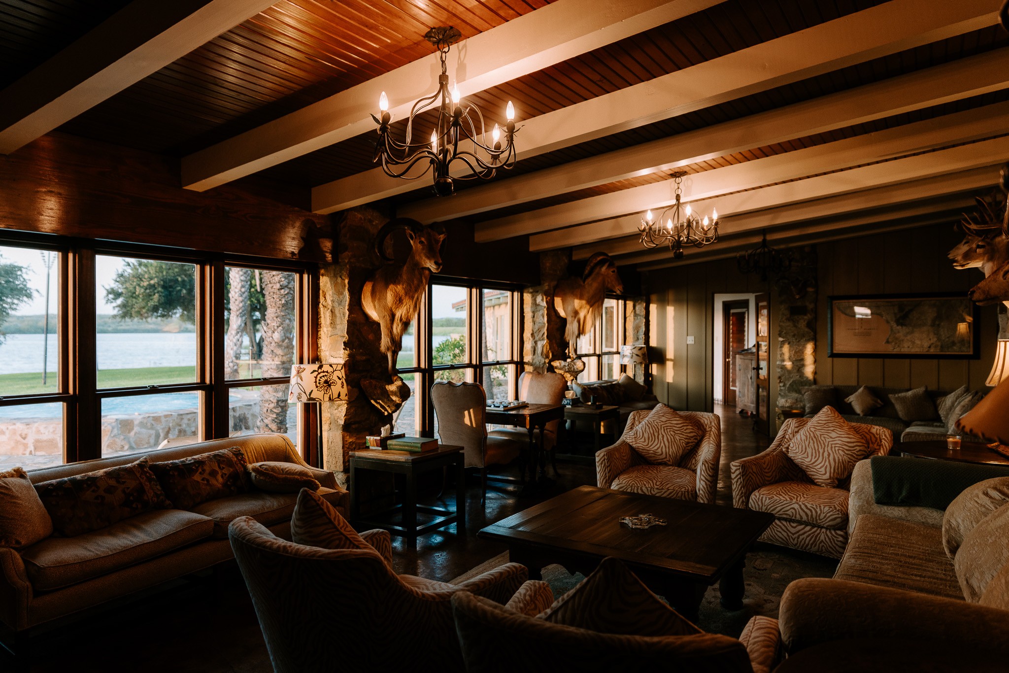A wood-beamed lodge living room with lake views through floor-to-ceiling windows
